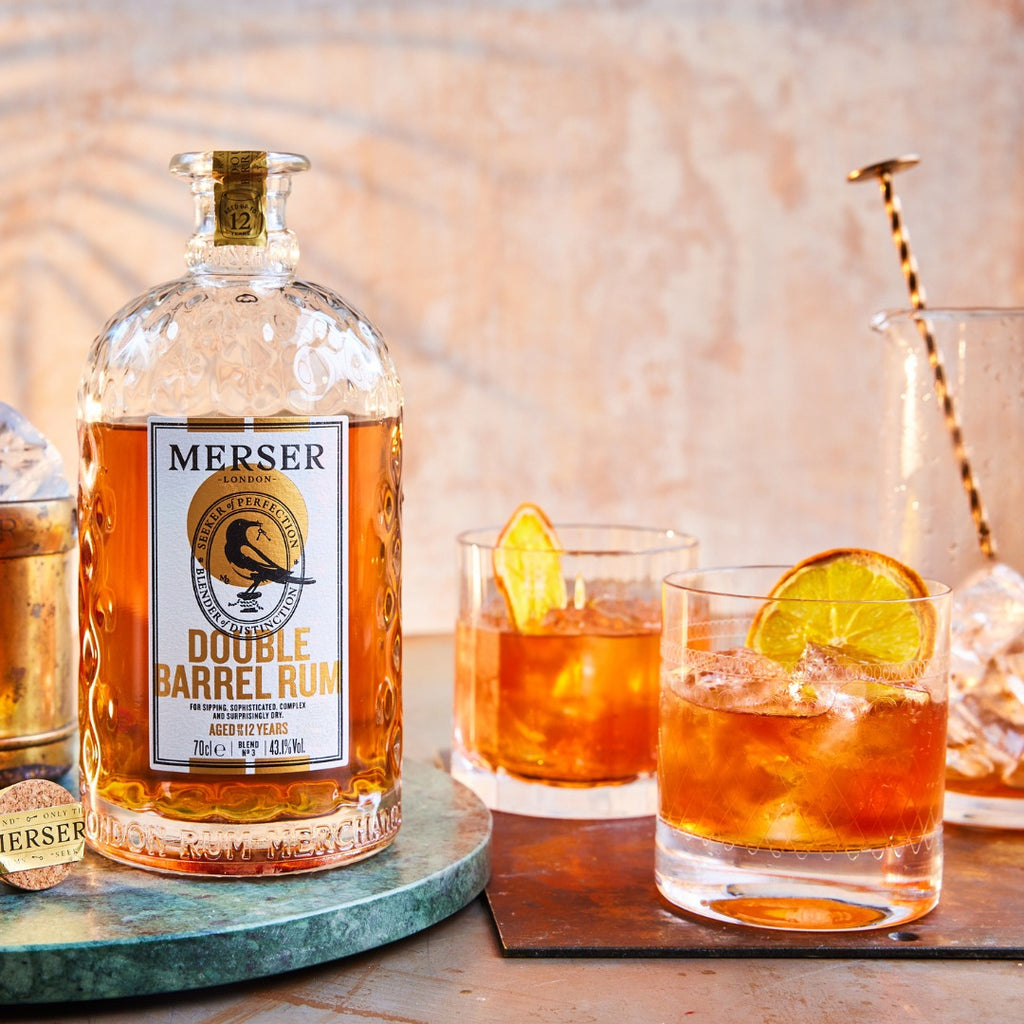Bottle of Merser Double Barrel Rum with two cocktails on a wooden surface.