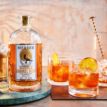 Load image into Gallery viewer, Bottle of Merser Double Barrel Rum with two cocktails on a wooden surface.