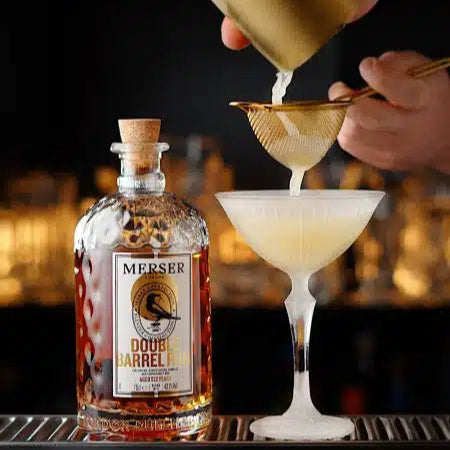 Bartender pouring a cocktail into a glass with a bottle of MeRSER DOUBLE BarreL RUM in the foreground.