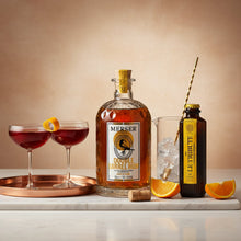 Load image into Gallery viewer, Bottle of Merser Double Barrel Rum and a Le Tribute Ginger Beer bottle with cocktails and oranges on a marble surface.