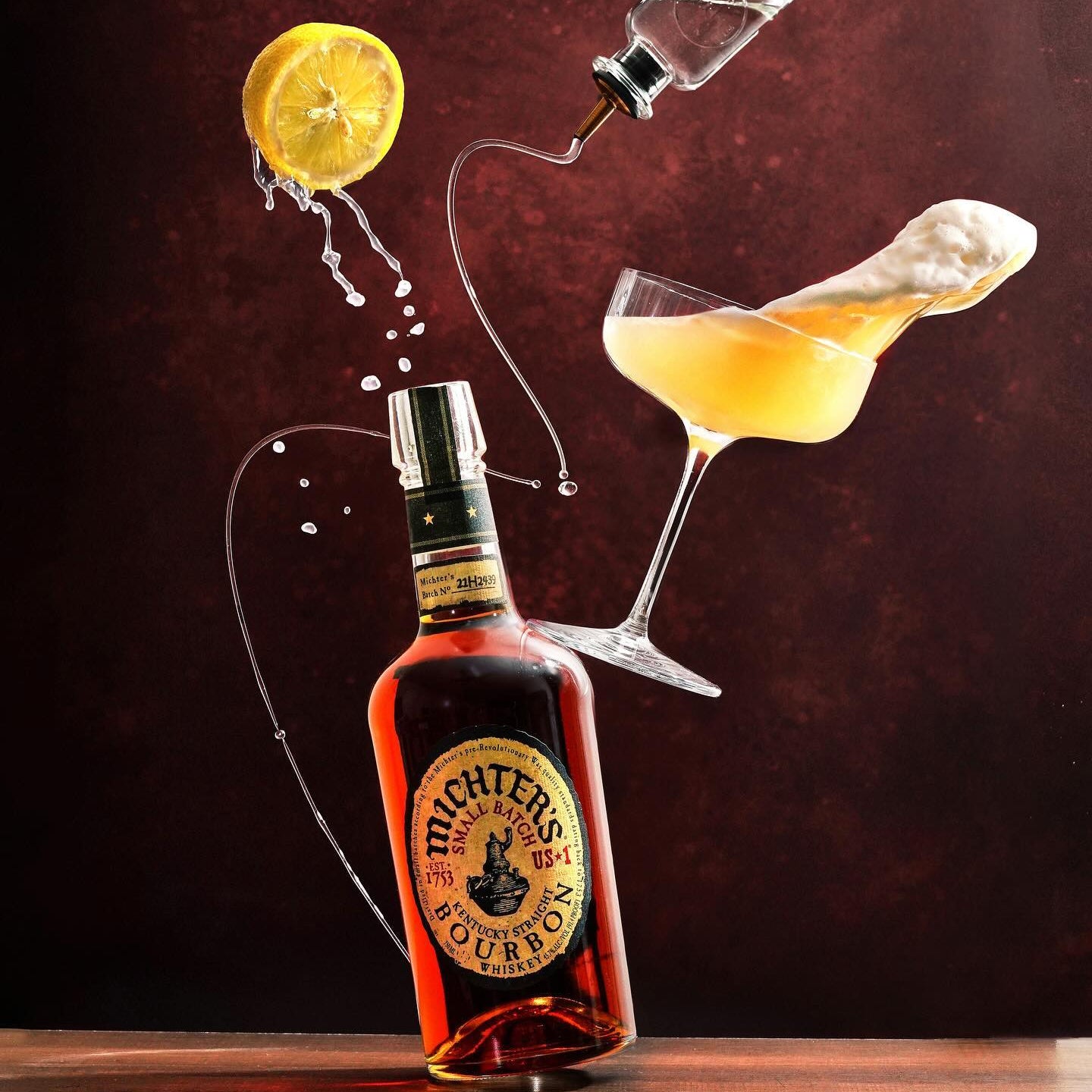 Load image into Gallery viewer, Bottle of Michter's bourbon with a cocktail and lemon twist on a dark background.
