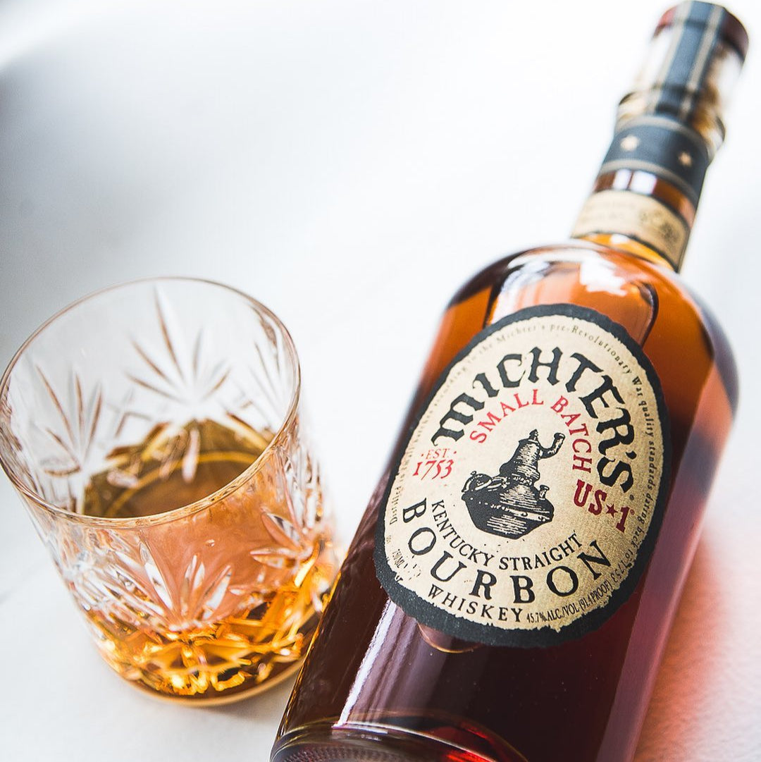 Load image into Gallery viewer, Bottle of Michter's bourbon whiskey with a glass of whiskey on a light background.