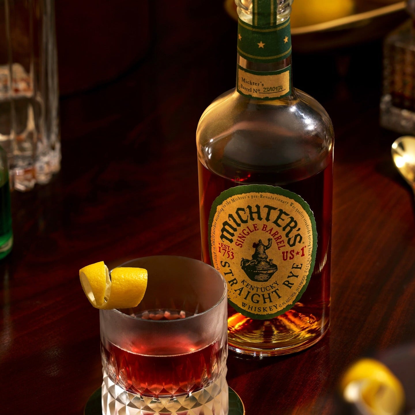 Load image into Gallery viewer, Michter's Michter’s US1 Single Barrel Rye Whiskey bottle with a cocktail garnished with a lemon twist on a wooden surface.