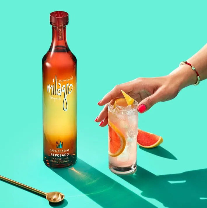 Load image into Gallery viewer, Milagro reposado tequila bottle with a cocktail and fruit on a teal background