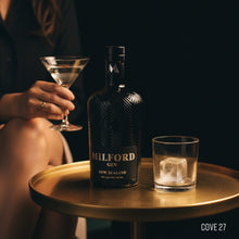 Load image into Gallery viewer, Milford Gin bottle with a glass and a cocktail on a table, against a dark background.