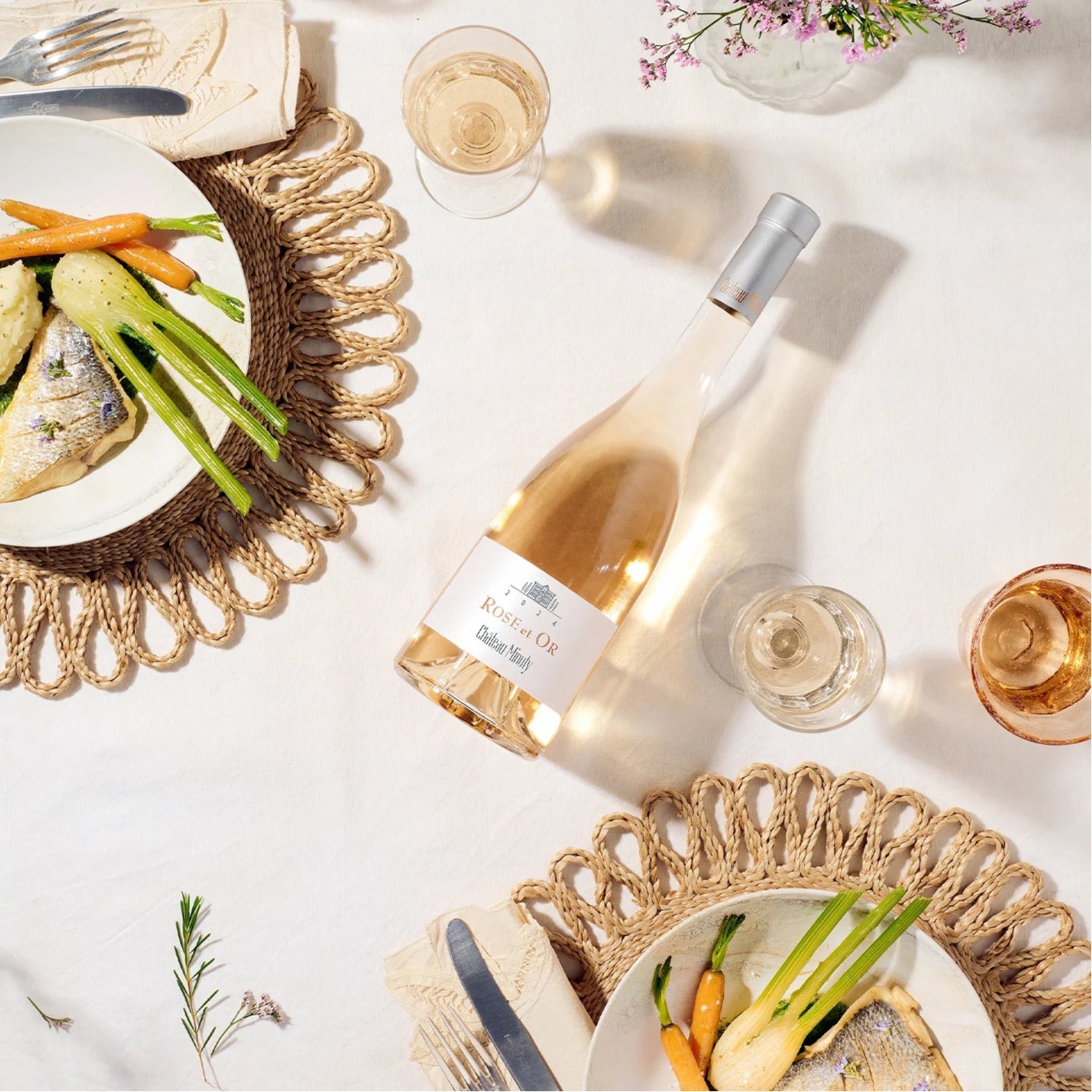 Load image into Gallery viewer, Table setting with wine bottle of Minuty Rose Et Or, plates of food, and glasses on a white surface.