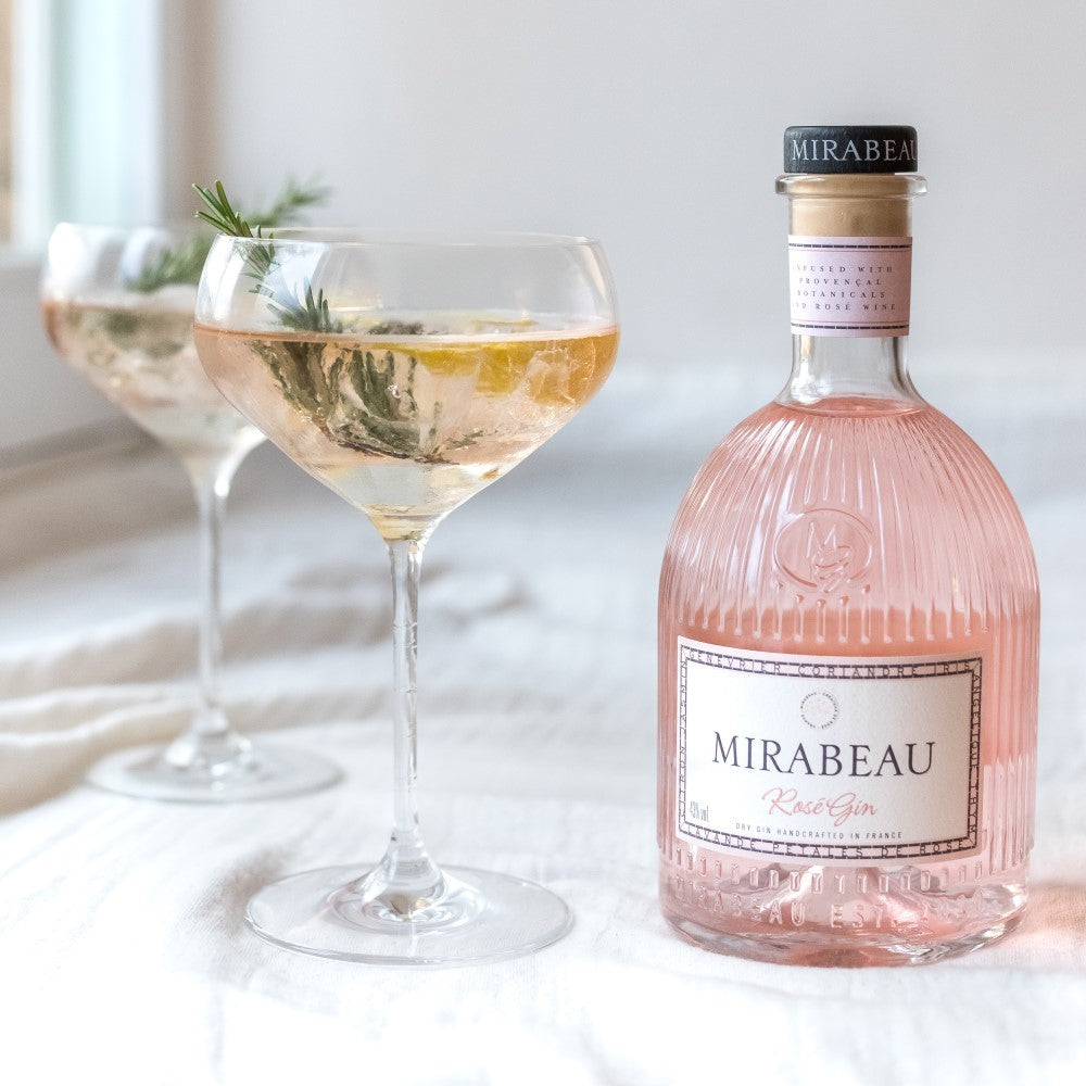 Bottle of Mirabeau Rosé Gin with two glasses filled with the pink gin on a light surface.