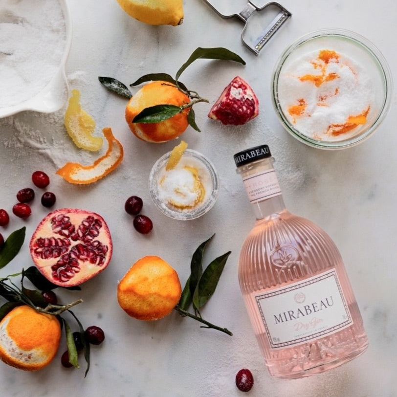 Pink bottle of Mirabeau Dry Rose Gin with fruits and a cocktail on a marble surface