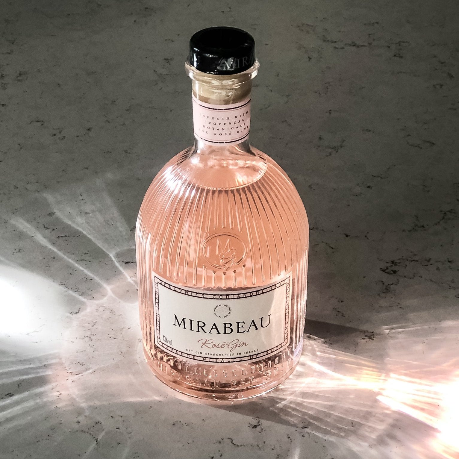 Load image into Gallery viewer, Pink bottle of Mirabeau Rosé Gin on a textured surface with soft lighting