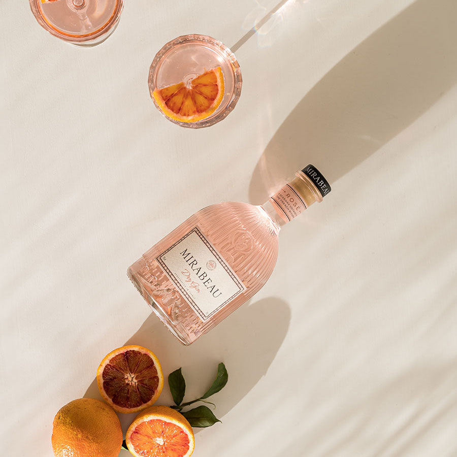 Load image into Gallery viewer, Pink bottle of Miraval Dry Rosé Gin with two glasses and oranges on a light background