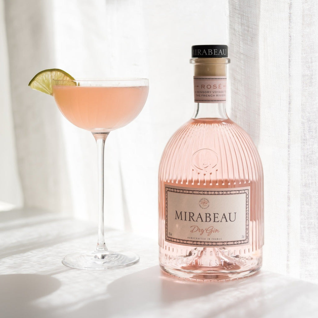 Bottle of Mirabeau Dry Rose Gin with a glass of pink cocktail on a white surface.