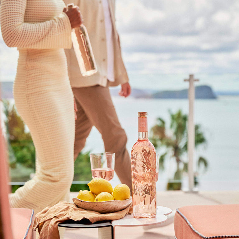 Load image into Gallery viewer, Bottle of Mirabeau Pure Provence Rosé wine on a table with lemons and a person in the background.