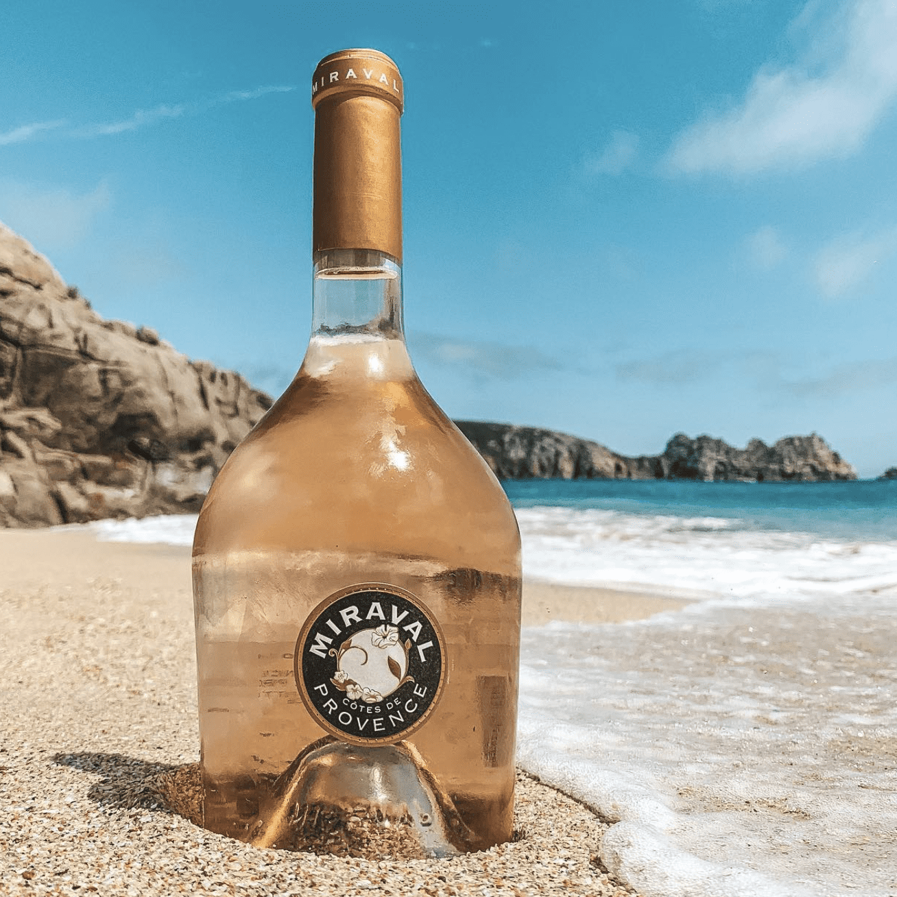 Load image into Gallery viewer, Miraval Provençal wine bottle on a beach with ocean and cliffs in the background