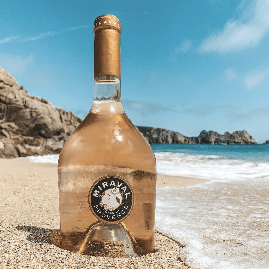Miraval Provençal wine bottle on a beach with ocean and cliffs in the background