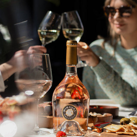 Load image into Gallery viewer, Bottle of Miraval Rosé wine with people enjoying a meal outdoors