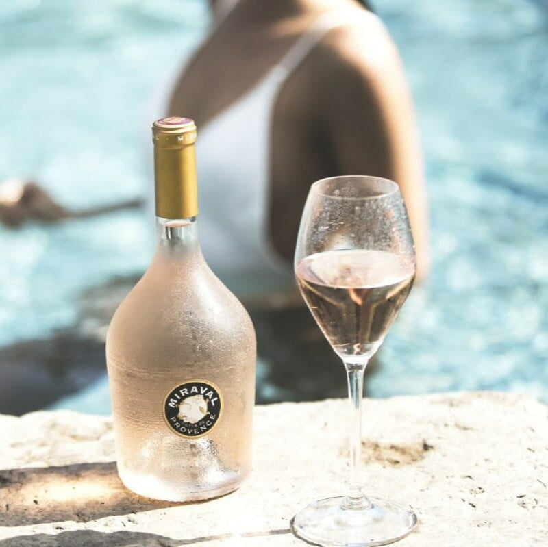 Load image into Gallery viewer, Bottle and glass of Miraval Provence rosé wine by a body of water.