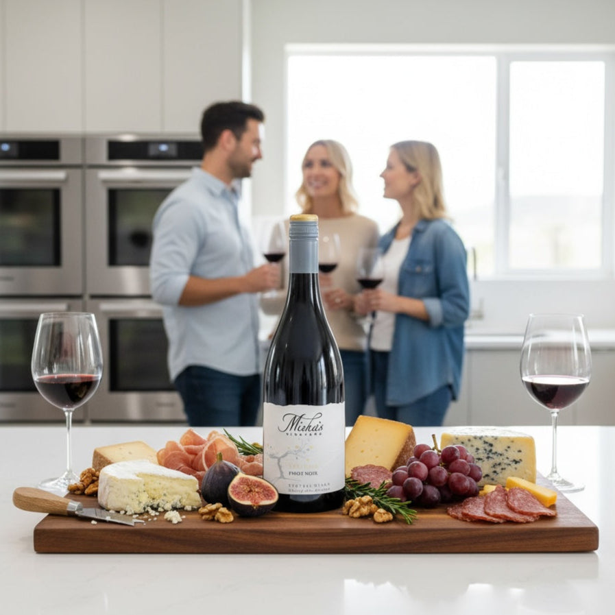 Load image into Gallery viewer, Mishas-Vineyard_Verismo_Pinot_Noir wine bottle on a charcuterie board with people in the background in a kitchen setting