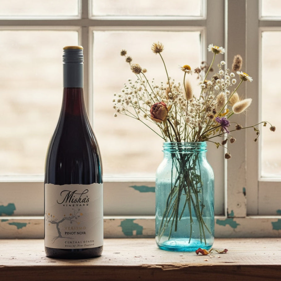 Load image into Gallery viewer, Mishas-Vineyard_Verismo_Pinot_Noir wine bottle with a label and a vase of flowers on a windowsill.