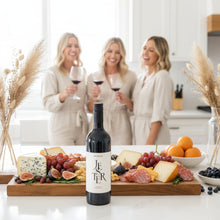 Load image into Gallery viewer, Three women in a kitchen holding wine glasses with a bottle of Mitolo-Jester-Shiraz-lifestyle wine and charcuterie board in the foreground.