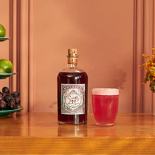 Load image into Gallery viewer, Bottle of Monkey 47 sloe gin with a glass of pink cocktail on a wooden bar counter, surrounded by fruits and flowers.