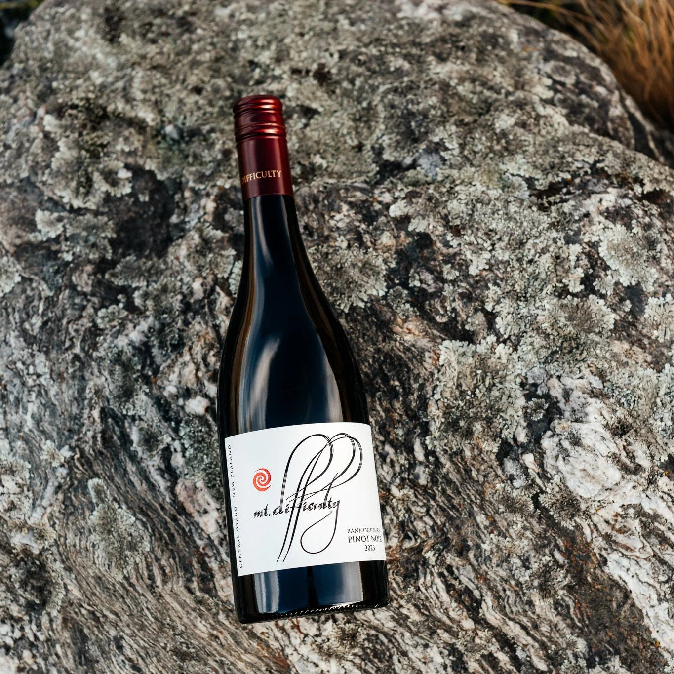 Load image into Gallery viewer, A bottle of Mt Difficulty Bannockburn Pinot Noir red wine placed on a large textured grey rock outdoors, with dry grass visible in the upper right corner.