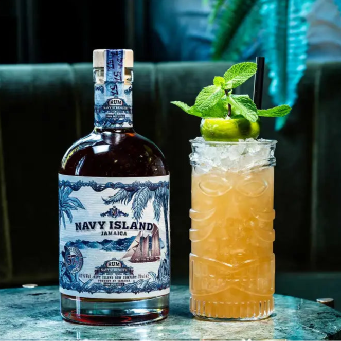 Bottle of Navy Island rum next to a cocktail with lime and mint on a dark background