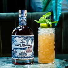 Load image into Gallery viewer, Bottle of Navy Island rum next to a cocktail with lime and mint on a dark background