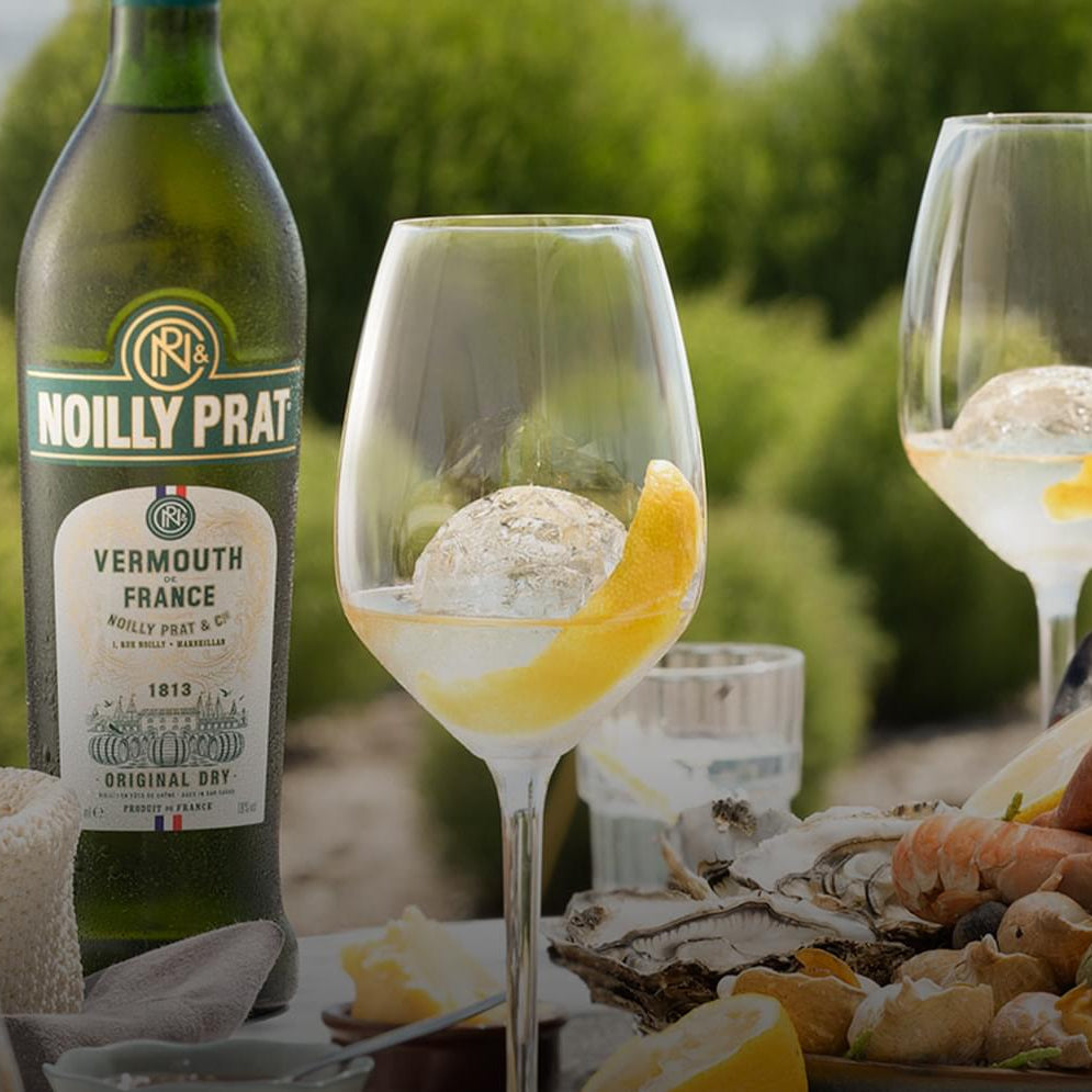 Load image into Gallery viewer, Noilly Prat Original Dry Vermouth bottle with two glasses of Vermouth on a table outdoors.