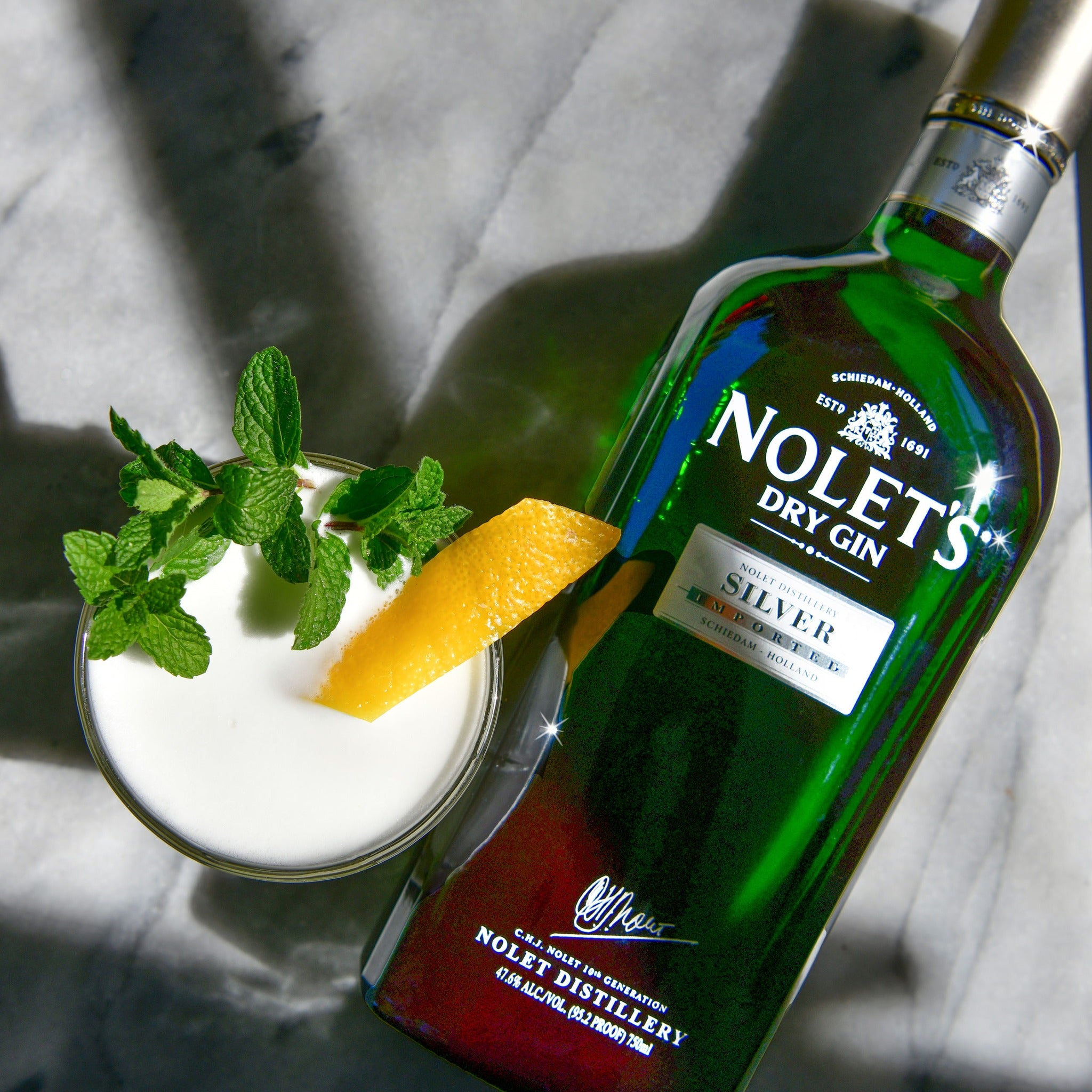 Load image into Gallery viewer, Nolet's Dry Gin bottle with a cocktail garnished with mint and orange on a marble surface