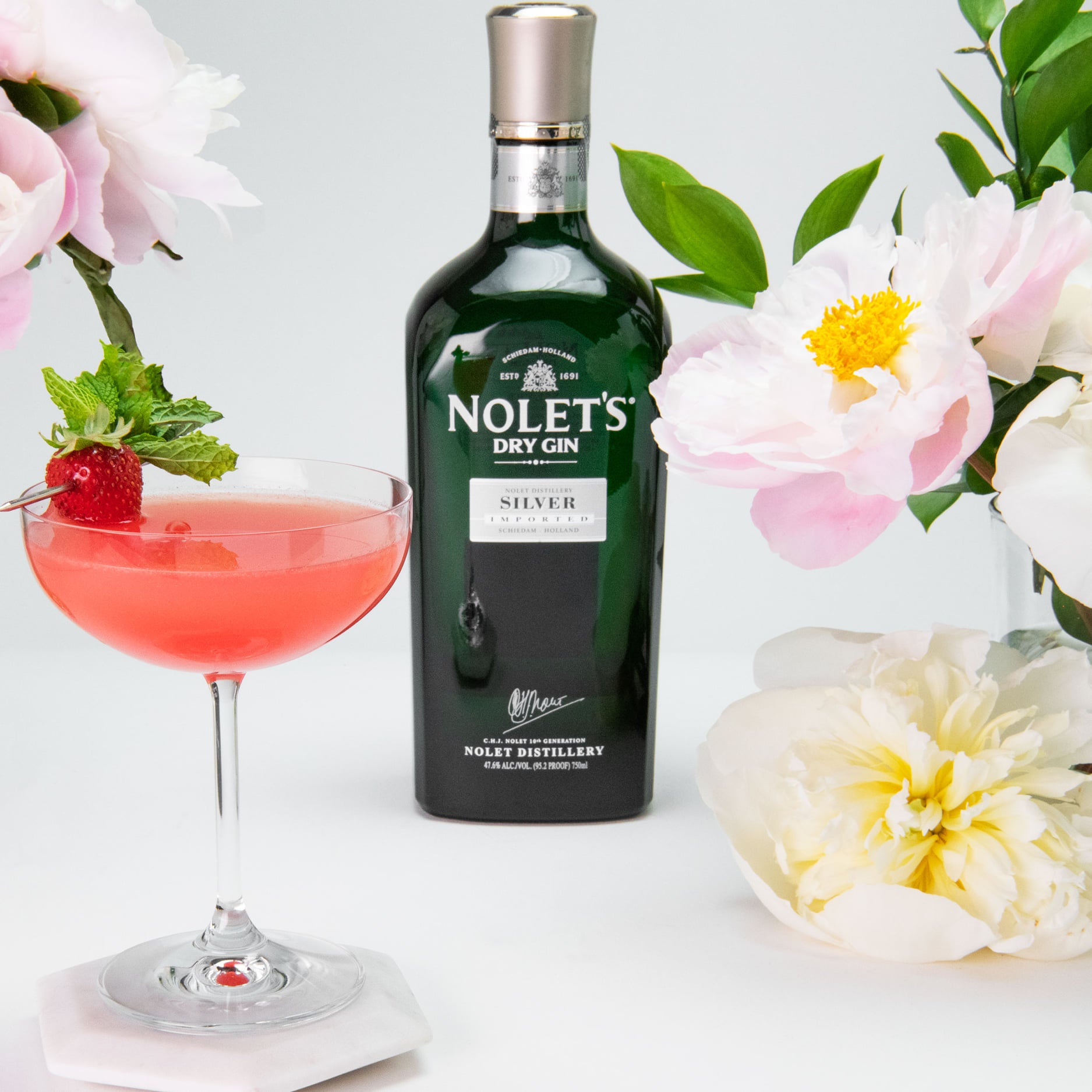 Load image into Gallery viewer, Nolet's Dry Gin bottle with a cocktail and flowers on a light background