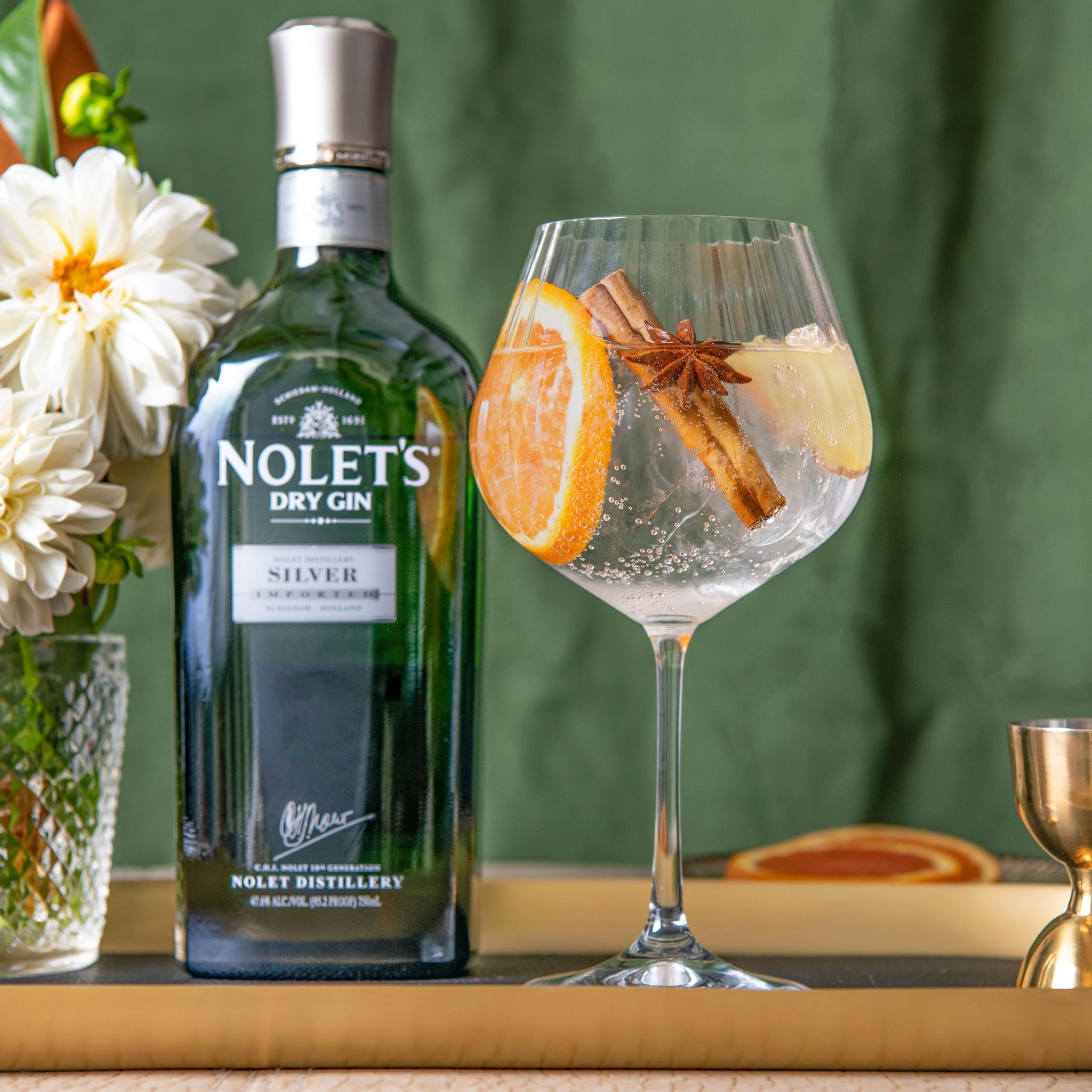 Load image into Gallery viewer, Nolet's Dry Gin bottle with a glass of gin and tonic garnished with an orange slice, star anise, and lemon peel on a wooden surface.