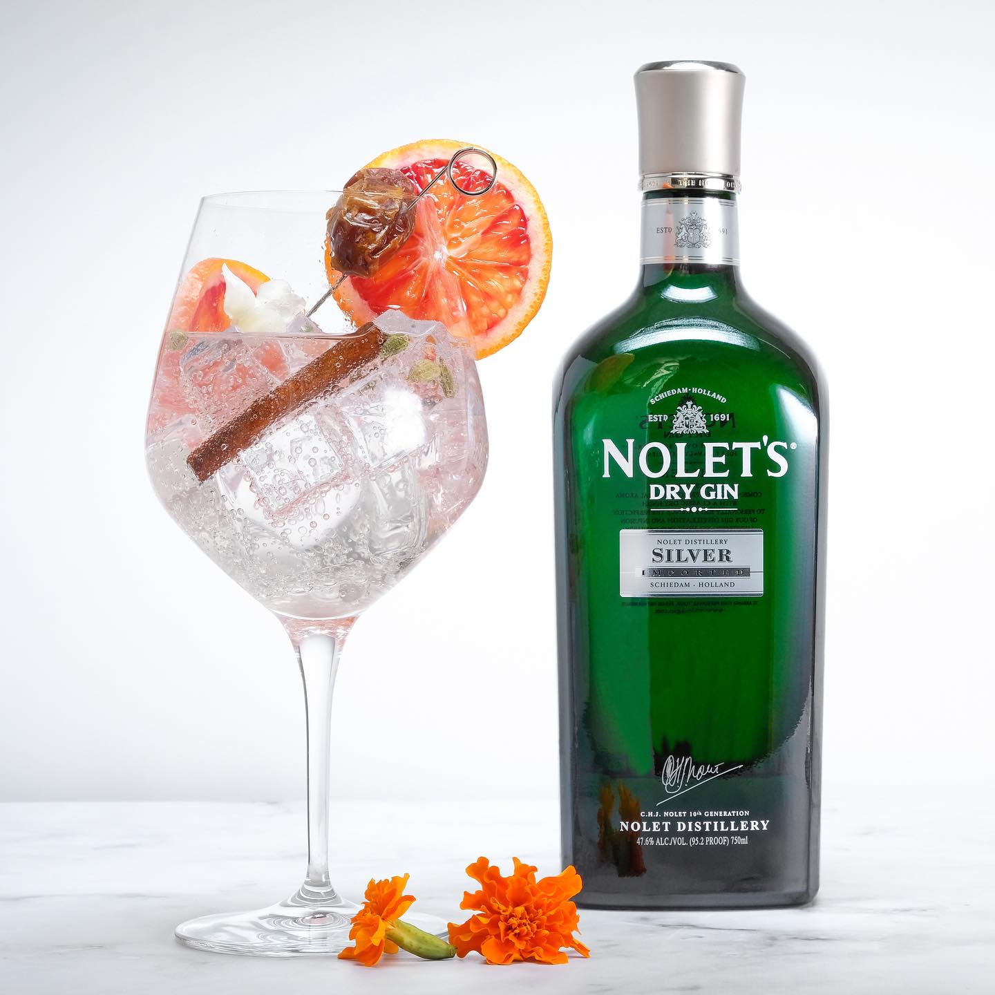 Load image into Gallery viewer, Nolet's Dry Gin bottle with a cocktail garnished with orange slices and a cinnamon stick on a white background