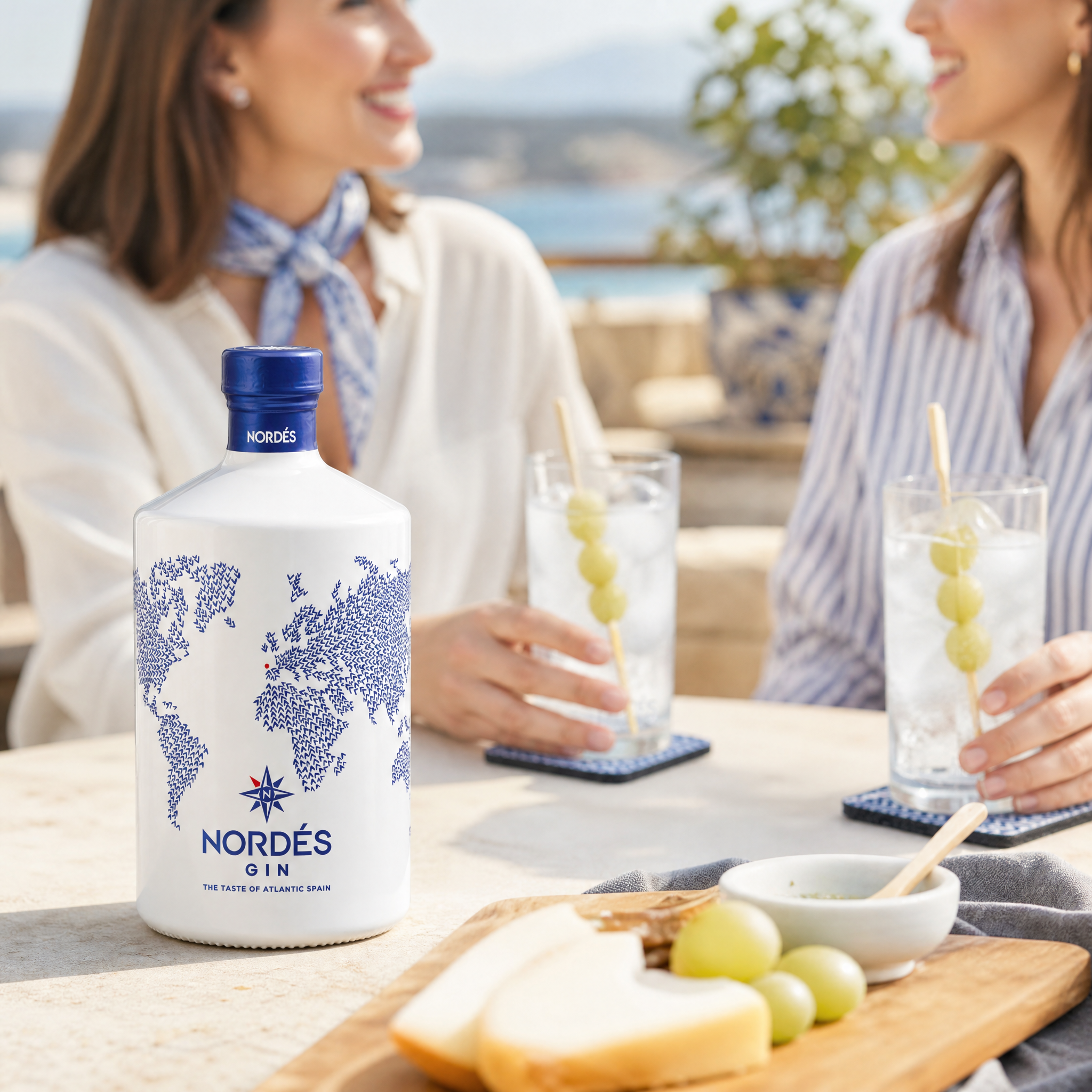 Load image into Gallery viewer, Women enjoying a bottle of Nordes Gin at a table in summer time.