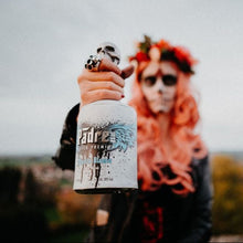 Load image into Gallery viewer, Person with red hair and sunglasses holding a bottle of Padre Blanco tequila outdoors.