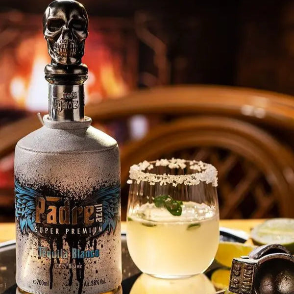 Padre Azul Blanco tequila bottle with skull design on a tray with a cocktail and limes.