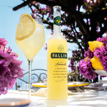 Load image into Gallery viewer, Pallini Limoncello bottle with a glass of limoncello on a table with flowers and lemon slices.
