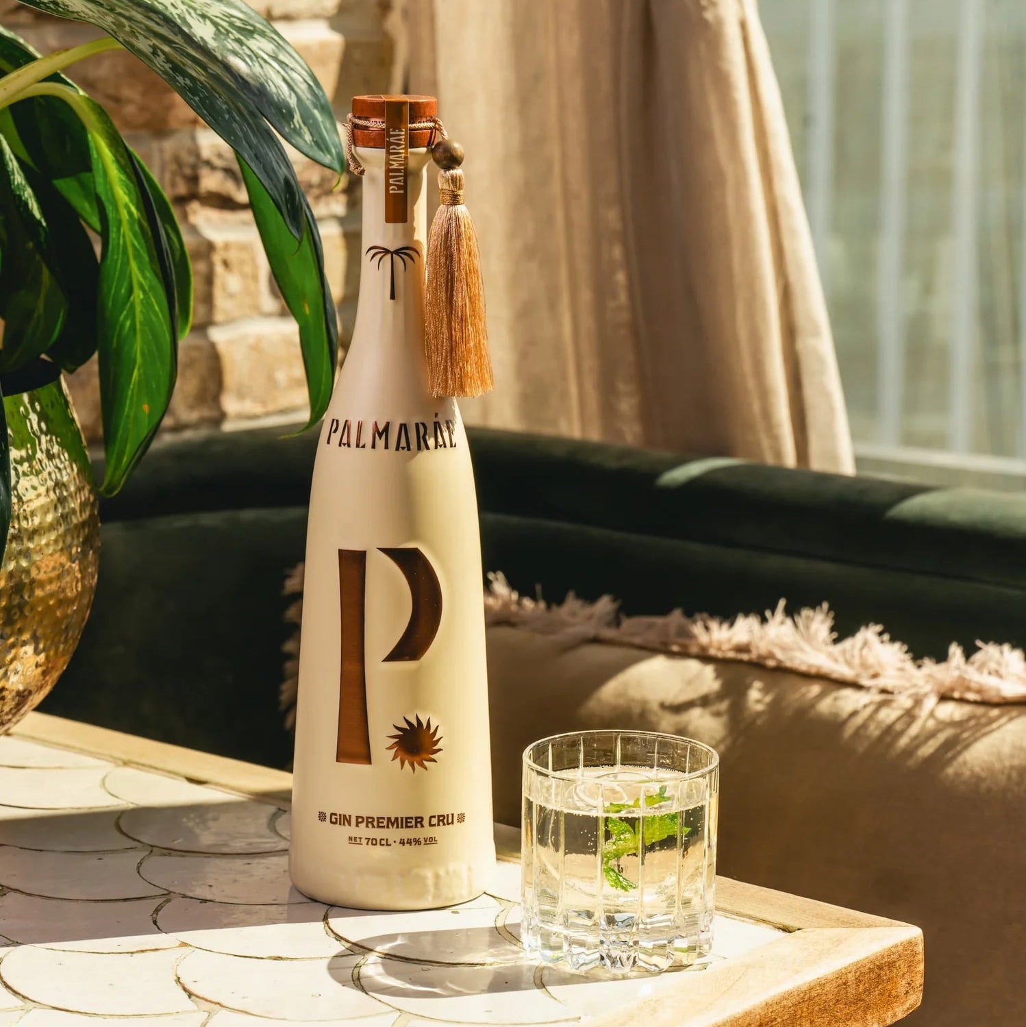 Load image into Gallery viewer, A bottle of Palmaráe Gin Premier Cru, styled on a wooden table next to a gin and tonic glass of water in a warm, sunlit indoor setting.