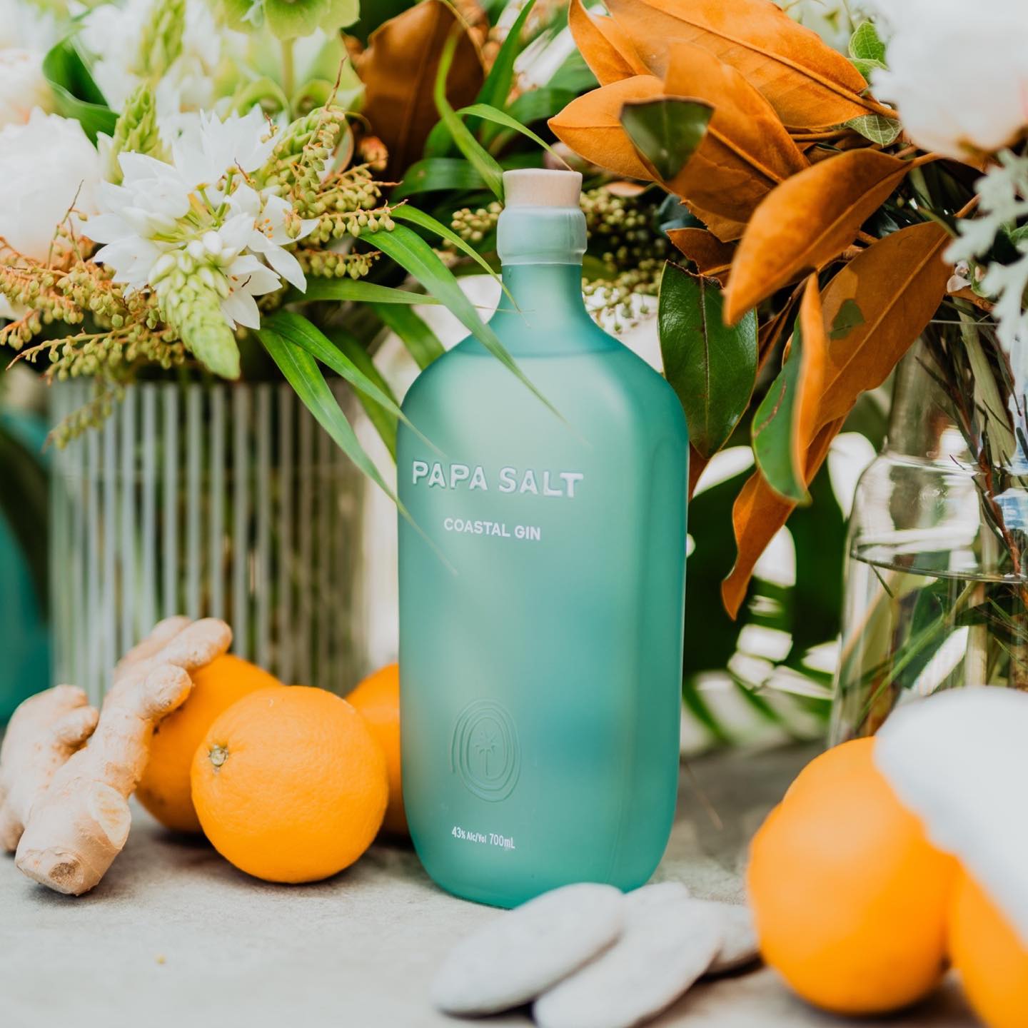 Load image into Gallery viewer, A bottle of Papa Salt Coastal Gin surrounded by oranges and tropical flowers