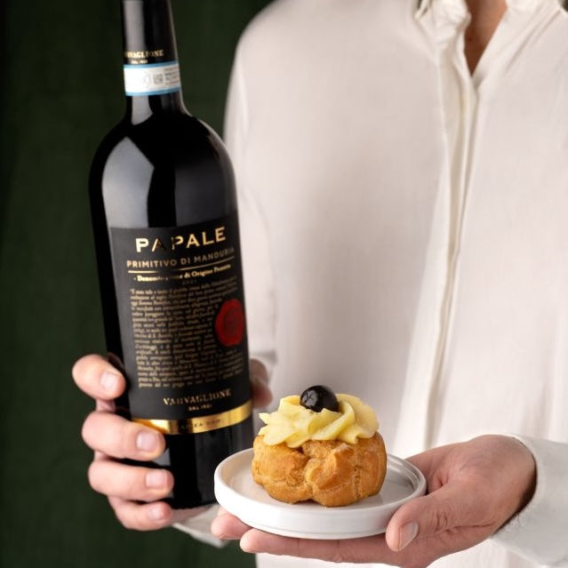 Load image into Gallery viewer, A man holding a bottle of Papale Oro Varvaglione Primitivo di Manduria red wine and small cake in the other hand