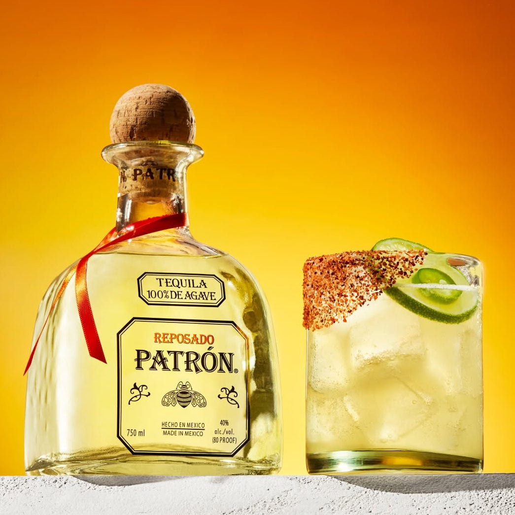 Load image into Gallery viewer, Patrón Reposado tequila bottle with a cocktail on an orange background