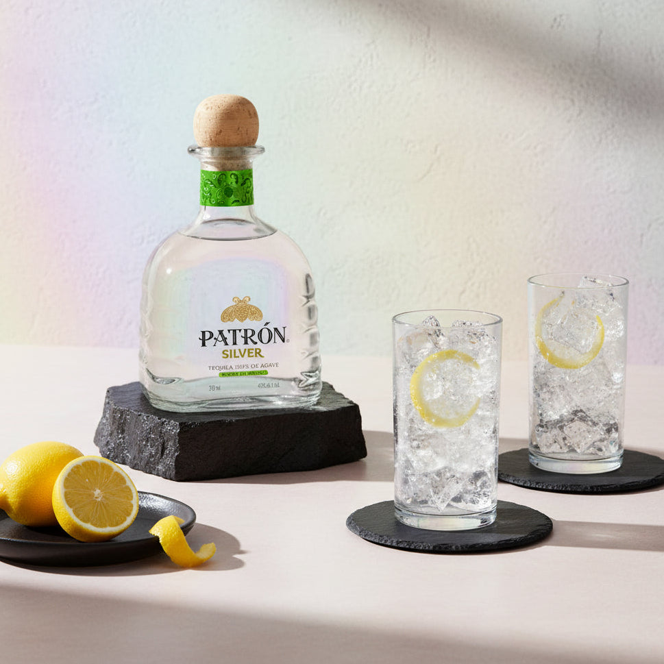 Load image into Gallery viewer, Patrón Silver tequila bottle with two glasses of ice and lemon slices on a light background