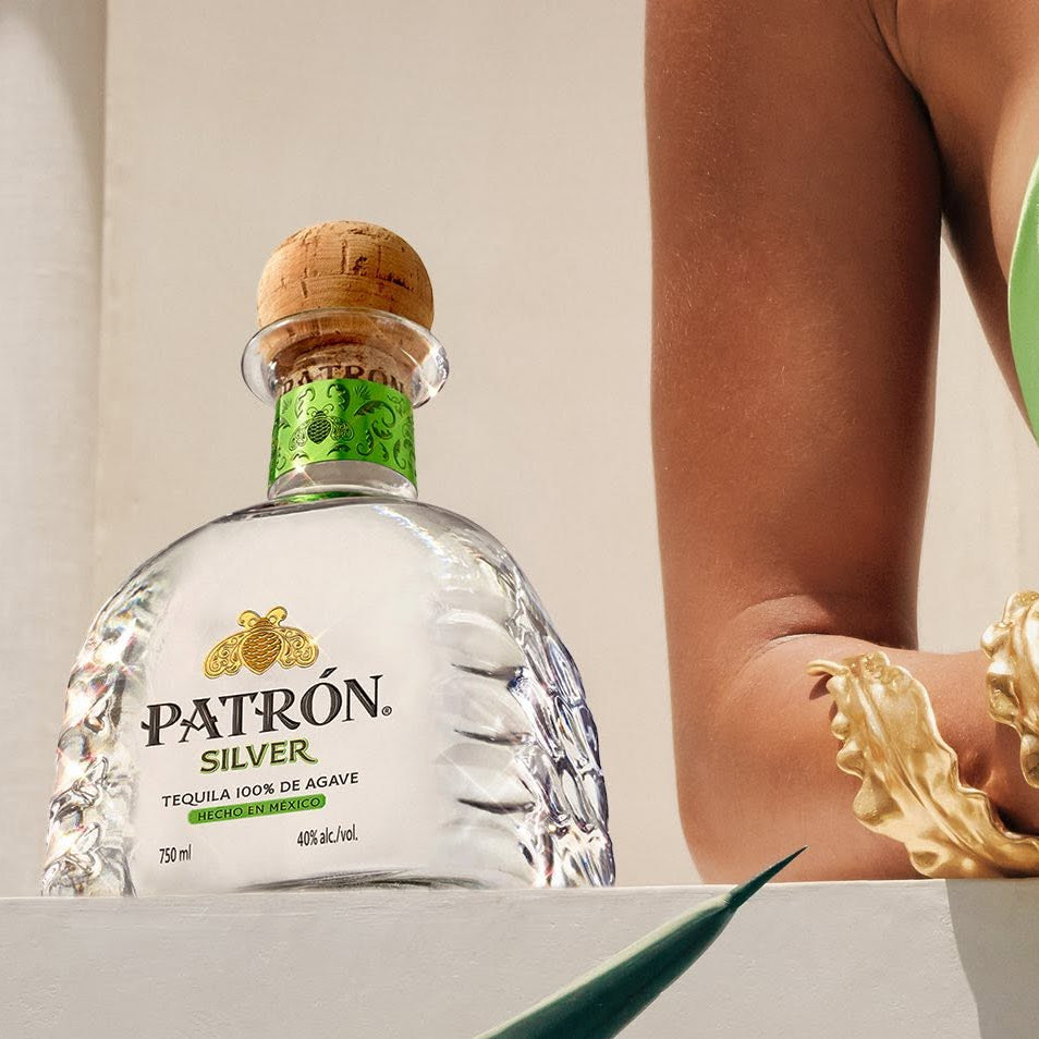 Load image into Gallery viewer, Patrón Silver tequila bottle with a person in a green bikini and gold bracelet on a neutral background.