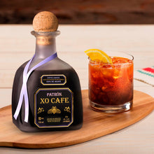 Load image into Gallery viewer, Patrón XO Cafe bottle with a glass of red cocktail on a wooden board