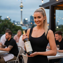 Load image into Gallery viewer, Woman holding a bottle of Pegasus Bay Minuetto Sauvignon Semillon wine in an outdoor setting with city skyline in the background