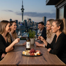 Load image into Gallery viewer, Group of people enjoying a bottle of Pegasus Bay Sauvignon Blanc white wine and cheese at a rooftop bar with a city skyline in the background