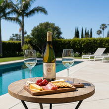 Load image into Gallery viewer, A bottle of Pegasus Bay Virtuoso Chardonnay wine next to a cheese and meat platter on  wooden outside table besire a swimming pool on a sunny clear day. 