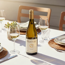 Load image into Gallery viewer, A bottle of white wine on a table with glasses, plates and some flowers.