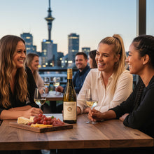 Load image into Gallery viewer, Three women enjoying a bottle of Pegasus Bay Virtuoso Chardonnay wine and cheese with a city skyline in the background