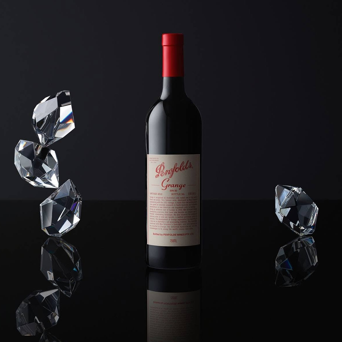 Load image into Gallery viewer, Bottle of Penfolds Grange shiraz wine with a red cap on a reflective black surface with ice cubes.