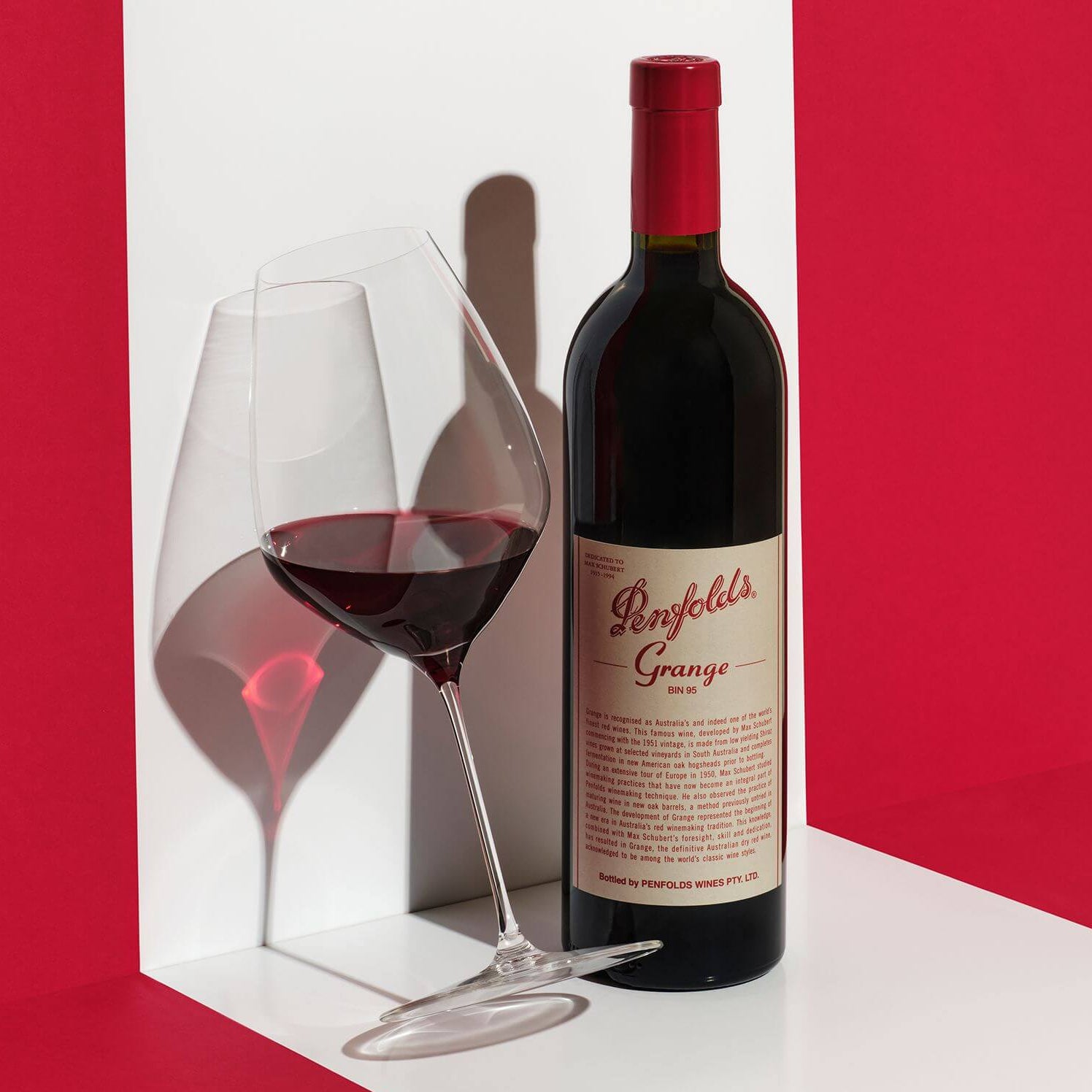 Load image into Gallery viewer, Penfolds Grange wine bottle with a glass of red wine on a white surface against a red background
